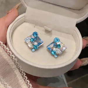 Primer plano de pendientes cuadrados con cristales azules y perla en su caja
