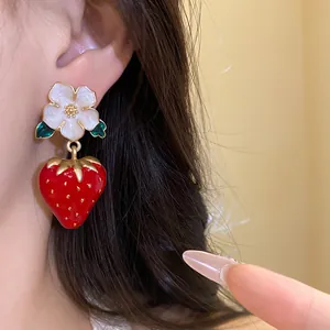 Close-up detail of sweet red strawberry and white flower drop earring worn on a model's ear