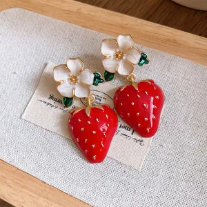 Close-up of sweet enamel strawberry and white flower drop earrings on a wooden tray.