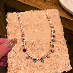 Elegant pearl necklace with colorful glass charms on a textured paper background