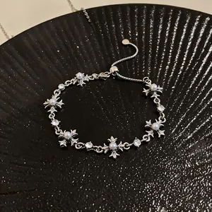 Detail of silver cross bracelet with pearls and rhinestones on black textured background