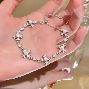 Close-up detail of a silver bracelet featuring pearl and iris cross charms held in hand