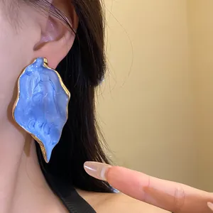 Detaillierte Nahaufnahme eines blauen Ohrrings in Blattform mit goldenem Rand am Ohr