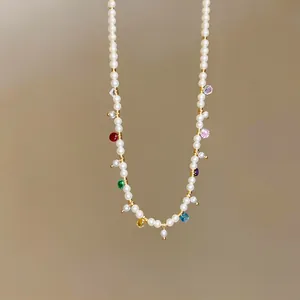 Detail view of a dainty pearl necklace with colorful glass charms in gold finish.