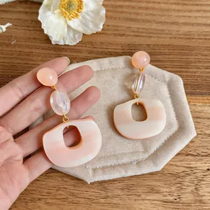 Close-up detail view of sweet pink resin oval earrings with gold-tone accents on a beige pad