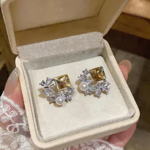 Detail shot of elegant yellow square zircon butterfly stud earrings with pearl in a jewelry box
