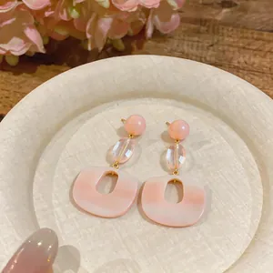 Detailed macro view of elegant pink resin drop earrings on a textured white plate with flowers.