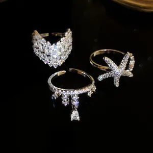 Close-up of three sparkling silver rings with starfish and heart designs on black surface.