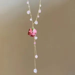 Close-up of elegant gold necklace with pink stones and dried rose pendant detail.