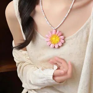 Dettaglio di una collana con grande ciondolo a margherita rosa e perline color pastello.