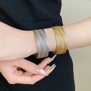 Detailed view of gold and silver woven metal cuff bracelets on a model's wrist.