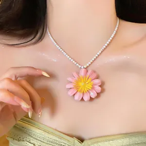Vista dettagliata di un ciondolo a margherita rosa su una collana di perle bianche