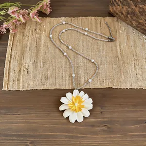 Dettaglio di una collana con ciondolo a margherita bianca e perle su stuoia rustica.
