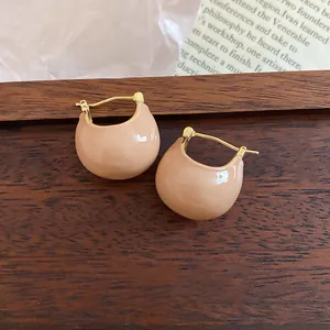 Close-up of minimalist beige enamel bean hoop earrings on a wood background.