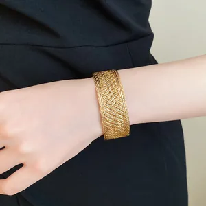 Detailed view of an elegant gold woven metal mesh cuff bracelet worn on the wrist.