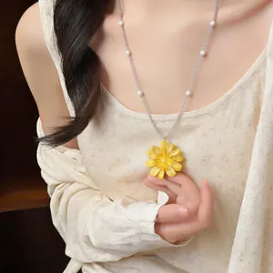 Primo piano di una collana con ciondolo a margherita gialla e perle indossata da modella