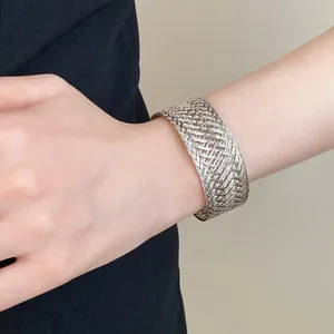 Close-up of a stylish wide silver woven metal cuff bracelet on a female wrist.