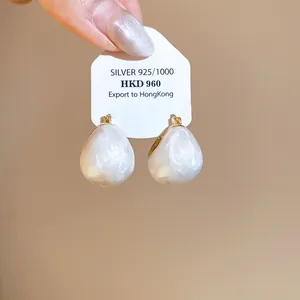 Close-up view of pearlescent white drip oil bean earrings with gold-plated finish on card.