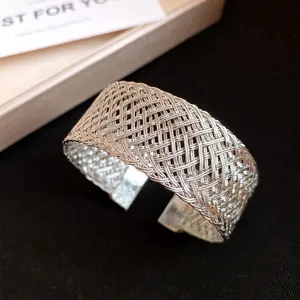 Close-up of a silver-toned woven metal open cuff bracelet with intricate mesh design