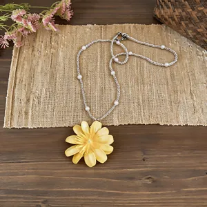 Primo piano dettagliato di una collana con pendente a margherita gialla e perle bianche.