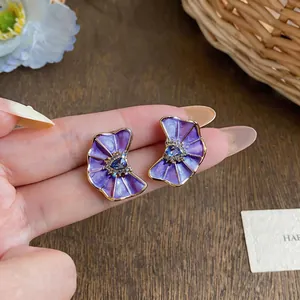 Close-up detail of purple enamel flower earrings with blue heart-shaped gem and crystals