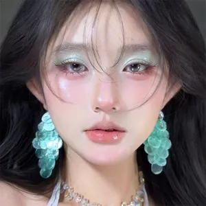 Close-up of a model wearing teal layered shell earrings with iridescent finish
