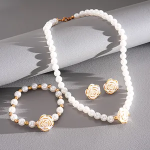 Elegant three-piece pearl jewelry set with white camellia charms on a gray textured surface