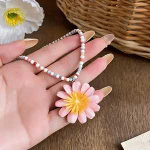 Primo piano dettagliato di un ciondolo a margherita rosa su una collana di perle.