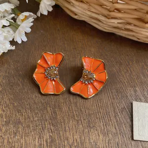 Close-up of vibrant orange enamel flower earrings with pleated texture and shiny rhinestones.
