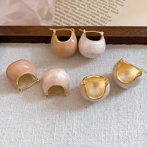Close-up of vintage gold-plated enamel hoop earrings in nude and white pearlescent.