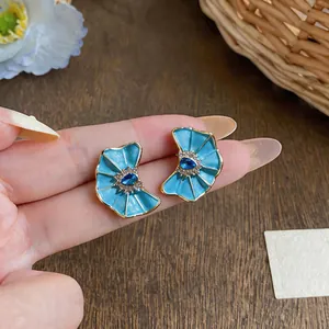 Detailed view of blue enamel fan-shaped stud earrings with crystal center held in hand