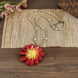 Dettaglio della collana con pendente a margherita rossa e perle su un tappetino rustico
