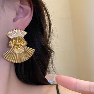 Close-up of a vintage-style gold pleated fan-shaped flower earring on a model's ear
