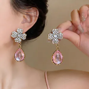 Dettaglio di orecchini vintage con fiore di strass e pendente a goccia in resina rosa.