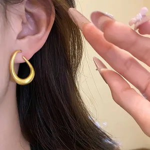 Nahaufnahme eines matten, goldfarbenen, ovalen Ohrrings im Vintage-Stil an einem Ohr
