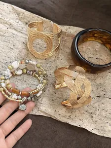 Detail of retro Maillard resin bangle and gold braided metal cuffs on textured stone background