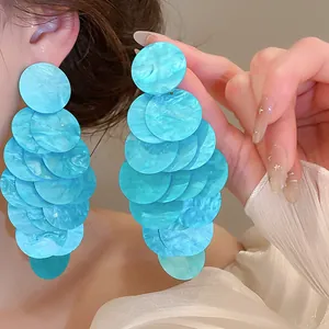 Detail view of large blue layered shell-style dangling earrings for a beach summer vacation