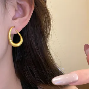 Nahaufnahme eines minimalistisch mattgoldenen, gedrehten ovalen Creolen-Ohrrings