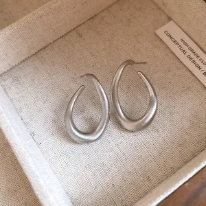 Detailansicht von silberfarbenen, gedrehten ovalen Ohrringen mit mattem Finish.