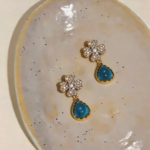 Primo piano di orecchini vintage dorati con pavé di fiori e pendenti a goccia blu