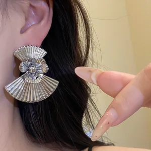 Detailed close-up of large silver fan-shaped metal flower earrings with pleated texture.