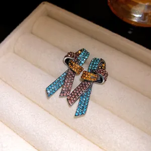 Primer plano de pendientes de nudo vintage con pedrería de colores y aguja de plata.