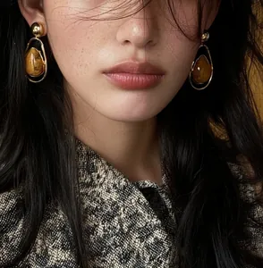 Close-up detail of vintage teardrop earrings with stone texture and gold frame on model
