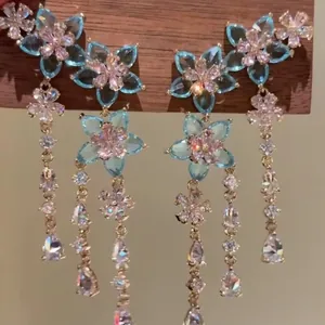 Detailed close-up of elegant blue zircon flower tassel earrings on wooden stand