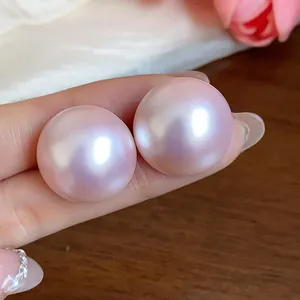 Primer plano de pendientes de perlas rosas redondas e iridiscentes sostenidos a mano