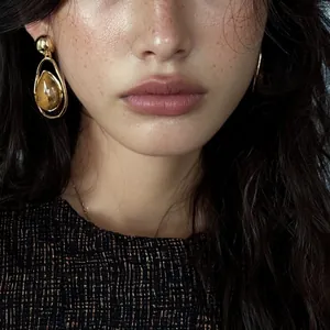 Detailed macro view of vintage gold-tone water drop pendant earrings on a model