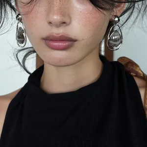 Close-up detail of silver-tone teardrop earrings featuring a grey stone on a freckled model.