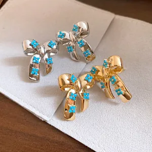 Macro shot of gold and silver bow earrings decorated with blue zircon flowers on grey background