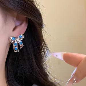 Detailed close-up view of silver bow stud earrings with blue floral zircon inlay on a model