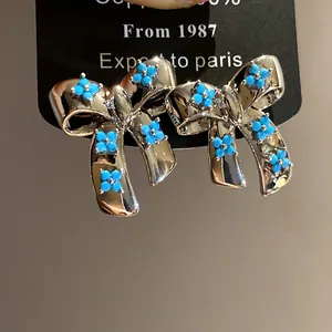 Detailed macro shot of silver bow stud earrings adorned with blue zircon flower accents